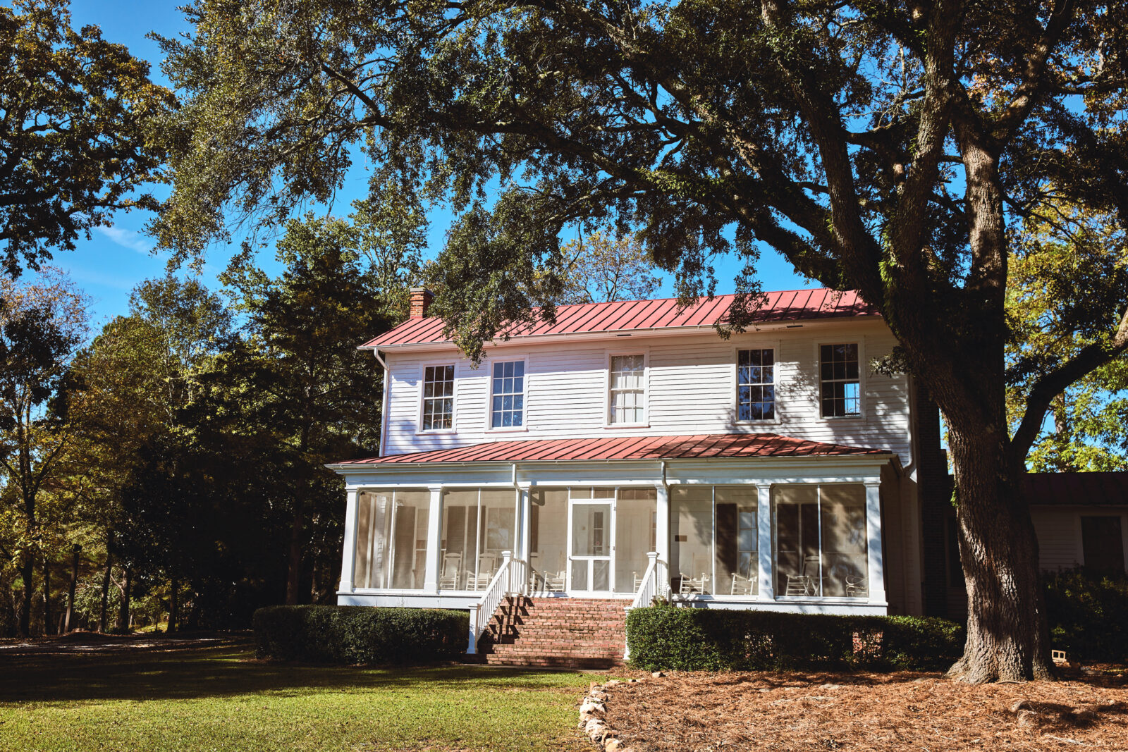 A white farmhouse with a red roof under some trees